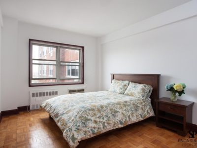 A bedroom with a bed, nightstand and window.